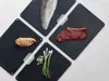 Four black cutting boards are arranged diagonally on a white surface, each with a different food item on it: a fish fillet, sliced chicken, a steak, and green onions with chopped garlic. Anteprima dell’immagine prodotto