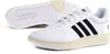 A pair of white Adidas Hoops 3.0 sneakers with black stripes and a cream-colored sole. One shoe is shown from the side, and the sole of the other shoe is visible in the background. Anteprima dell’immagine prodotto