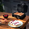 A waffle maker is shown in use on a wooden table, with finished waffles and ingredients nearby. Produktbild-Vorschau