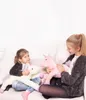 Two young girls sitting on a couch, each holding a plush unicorn toy. Voir les images du produit