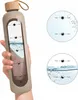 A hand holding a beige water bottle with measurement markings and water inside. Two circular insets show close-ups of the measurement markings with water levels and times. Produktbild-Vorschau