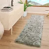 A fluffy gray rug is placed on a wooden floor next to a white dresser. A large window with a mountain view is in the background. Produktbild-Vorschau