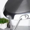 Close-up view of the handle attachment of a stainless steel pan, with a potted plant in the background. Voir les images du produit