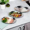 Three oval serving platters are arranged on a countertop. The platters are made of stainless steel and are empty, except for one which contains a grilled fish and vegetables, and another which contains sliced meats and broccoli. Produktbild-Vorschau