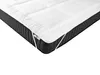 A close-up view of a white mattress topper placed on a dark gray mattress. Náhled obrázku produktu