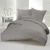A neatly made bed with taupe bedding, set against a bright, minimalist background with white shutters. Produktbild-Vorschau