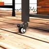 Close-up of a black caster wheel with a brake attached to the leg of a dark gray metal grill cart, resting on a wooden deck. Produktbild-Vorschau
