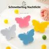 A collection of butterfly-shaped night lights arranged on a white surface with small pom-poms. Produktbild-Vorschau