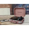 A pink suitcase-style record player is open on a wooden table, with a stylus and a small notepad next to it. Náhled obrázku produktu