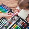 A close-up of a child's hand holding a small tube of pink paint, being offered by an adult's hand, with an open art set in the background. Produktbild-Vorschau