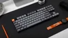A keyboard and other desk accessories are arranged on a black desk mat. Produktbild-Vorschau