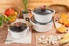 A collection of white pots with wooden handles and glass lids, arranged on a wooden surface with various ingredients like pumpkins, mushrooms, and corn. Produktbild-Vorschau