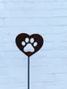 A rusty metal garden stake with a heart shape and a paw print cut out, set against a white brick wall. Produktbild-Vorschau