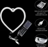 A white heart-shaped neon light with its battery pack and USB cable shown separately against a black background. Text overlays describe the power options. Voir les images du produit