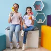 Two young girls are sitting on a storage bench, each drinking from a colorful water bottle. Náhled obrázku produktu
