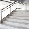 A close-up view of a modern staircase with white tiled steps and a silver metal handrail with frosted glass panels. Produktbild-Vorschau