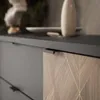 A close-up view of a modern kitchen cabinet with a dark countertop and a decorative wooden drawer front. Produktbild-Vorschau