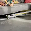 A person is reading a book on a couch while a floor cleaner is cleaning underneath the couch. Anteprima dell’immagine prodotto