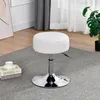 A white adjustable stool on a rug next to a stack of books and a plant. Produktbild-Vorschau