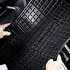 Hands holding a black rubber car floor mat with water droplets on it. Produktbild-Vorschau