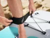 A person is securing an ankle strap to their leg, which is attached to a paddleboard. Produktbild-Vorschau