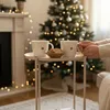 A cozy Christmas scene with a side table holding two mugs and cookies, in front of a decorated Christmas tree and fireplace. Produktbild-Vorschau