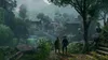 Two people walk down a path towards a village nestled in a lush, misty forest. Produktbild-Vorschau