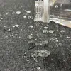 Water being poured from a clear bottle onto a dark, textured surface, creating droplets. Produktbild-Vorschau
