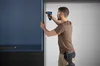A man is using a cordless drill to attach a piece of trim to a cabinet. Náhled obrázku produktu