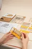 Hands assembling a wooden model tram, with instructions and parts laid out on a table. Produktbild-Vorschau