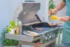A person is grilling food on a gas grill outdoors. Náhled obrázku produktu