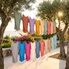 Bunte T-Shirts aus Bambus-Viskose-Jersey hängen an Wäscheleinen zwischen Olivenbäumen. Die hängenden Shirts zeigen den weichen, fließenden Fall und die Dehnbarkeit des Bambus-Stoffes im warmen Sonnenlicht. Produktbild-Vorschau