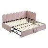 A pink upholstered daybed with a pull-out trundle bed is shown from a slightly elevated side angle against a white background. The daybed has a scalloped headboard and sides. The wooden slats of the main bed frame are visible, and the metal mechanism for t Podgląd zdjęcia produktu