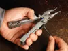 A person's hands are holding and using a Leatherman multi-tool to work on a wire. Produktbild-Vorschau