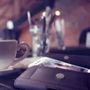A close-up of a smartphone in a wallet case next to a cup of coffee on a table. Produktbild-Vorschau