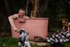 A man is sitting in a large terracotta bath bucket outdoors, playing with a dog. Náhled obrázku produktu
