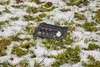 A black protective box with cables and connectors sits on the ground, partially covered in snow and grass. Produktbild-Vorschau