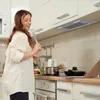 A woman is in a modern kitchen, singing into a whisk while looking at a laptop. Voir les images du produit