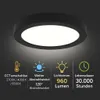 A black circular LED ceiling light is shown from a slightly angled front view, with a dark background. Below the light, there are four icons with accompanying German text describing the product's features. Náhľad obrázku produktu