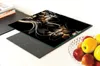 A glass cutting board with a floral design is placed on top of a black induction cooktop. A bowl of fruit is visible to the right. Produktbild-Vorschau
