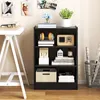 A black three-shelf bookcase filled with various items, placed next to a white desk. Náhled obrázku produktu