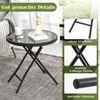A round black folding table with a glass top, placed on a rug next to a sofa. The image also includes close-up shots highlighting the table's features. Produktbild-Vorschau