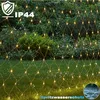 A net of warm white LED lights is draped over a garden setting with grass and bushes. Náhled obrázku produktu