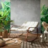 A rocking chair with cushions is placed on a wooden deck, surrounded by plants and lanterns, creating a cozy outdoor seating area. Voir les images du produit