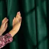 A person's hands are touching a dark green velvet curtain, with shadows cast on the fabric. Produktbild-Vorschau