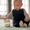 A baby sitting on a blanket reaching for a baby bottle. Produktbild-Vorschau