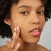 A close-up shot of a woman applying a cream to her face. Produktbild-Vorschau