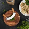 A kitchen scene with a cutting board, a mezzaluna knife, herbs, rice, and a plate of chicken. Anteprima dell’immagine prodotto