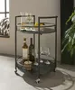 A black metal bar cart filled with wine bottles, glasses, and fruit is placed in a room with a window and a plant. Produktbild-Vorschau