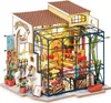 A miniature model of a flower shop with a greenhouse attached, illuminated by interior lights. Náhled obrázku produktu